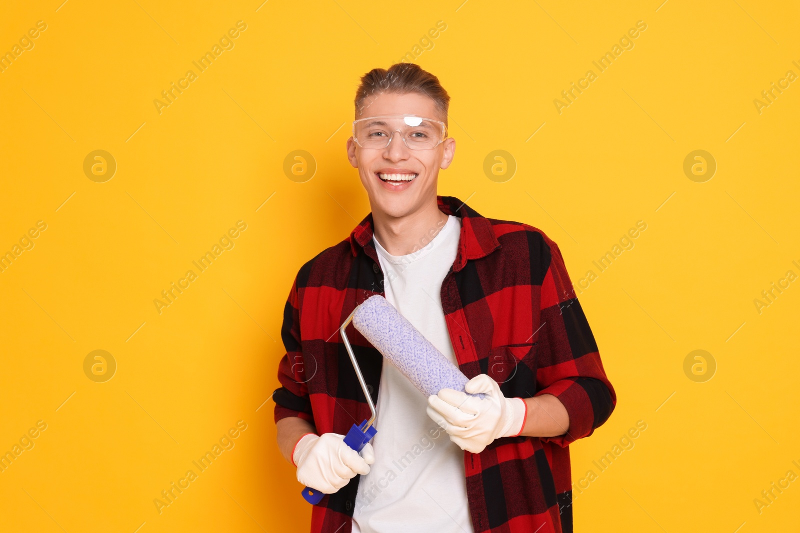 Photo of Portrait of young decorator with paint roller on orange background