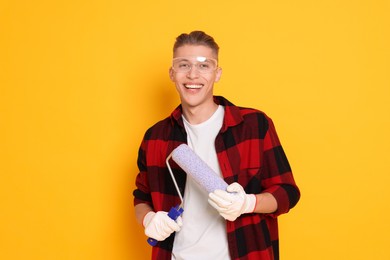 Photo of Portrait of young decorator with paint roller on orange background