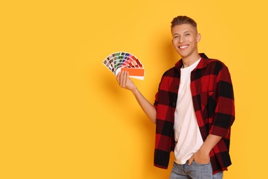 Photo of Portrait of young decorator with color palettes on orange background, space for text