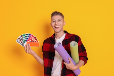 Photo of Young decorator with color palettes and rolls of wallpaper on orange background