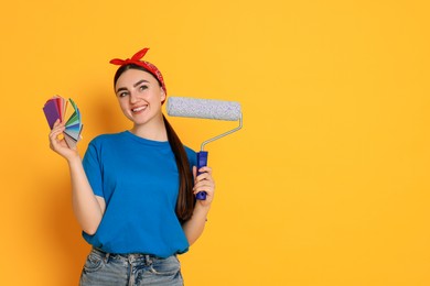 Photo of Portrait of young decorator with color palettes and paint roller on orange background, space for text