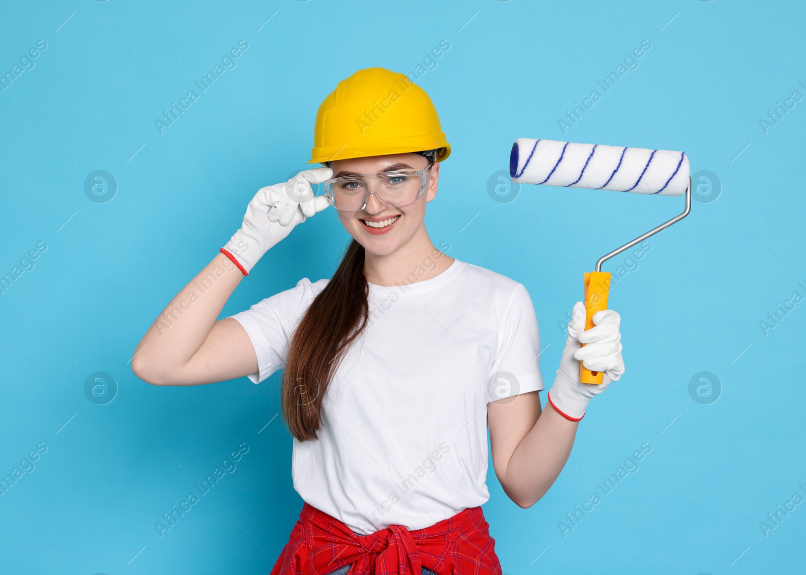 Photo of Portrait of young decorator with paint roller on light blue background