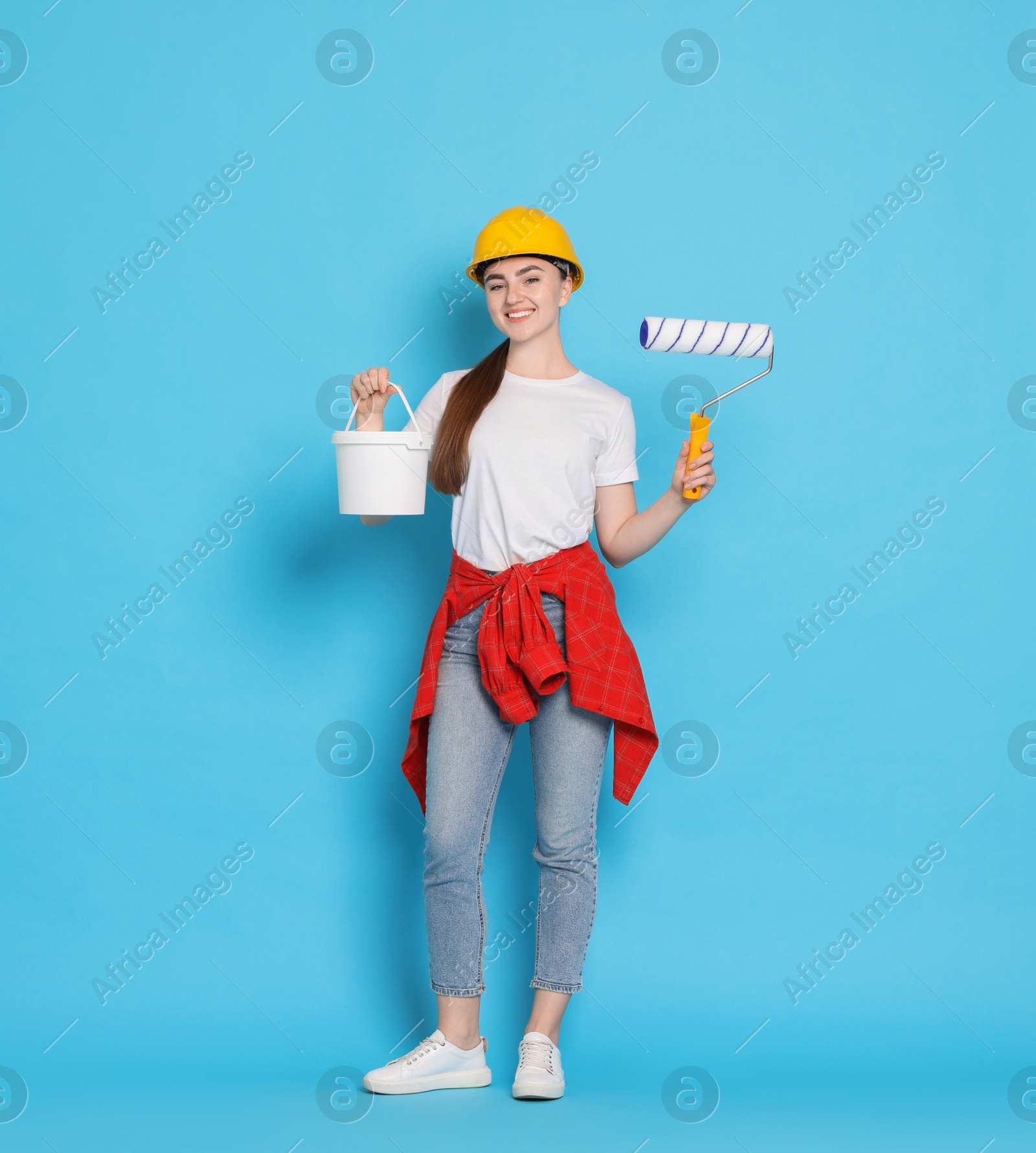 Photo of Young decorator with paint roller and bucket on light blue background