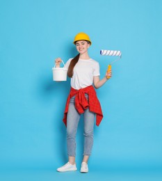 Photo of Young decorator with paint roller and bucket on light blue background