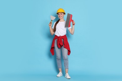 Photo of Young decorator with putty knives on light blue background