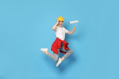 Young decorator with paint roller jumping on light blue background