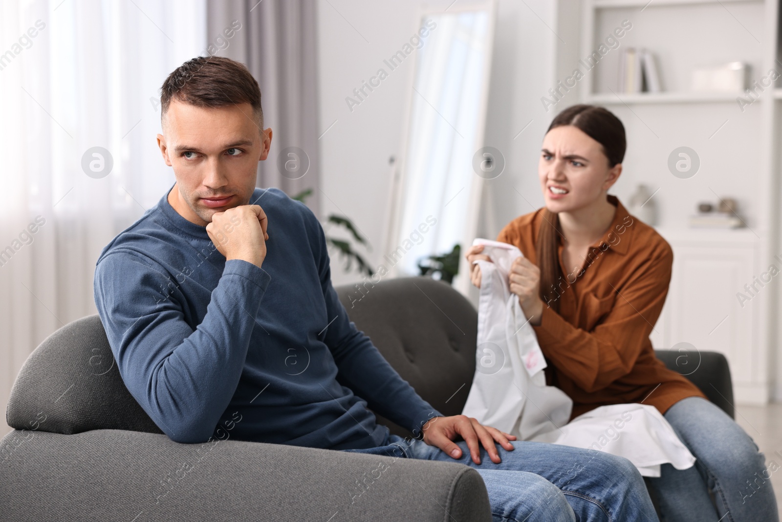 Photo of Emotional wife showing shirt with lipstick marks as proof to her unfaithful husband at home