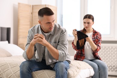 Photo of Puzzled wife finding mistress bra and unfaithful husband at home, selective focus