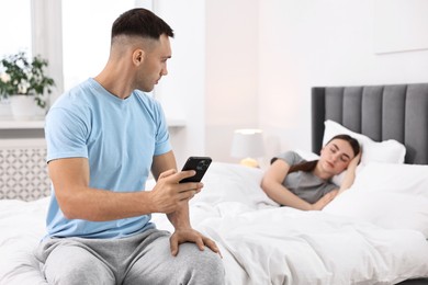 Photo of Jealous man checking wife's smartphone while she sleeping in bedroom, selective focus