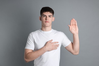 Photo of Man making promise with raised hand on grey background. Oath gesture