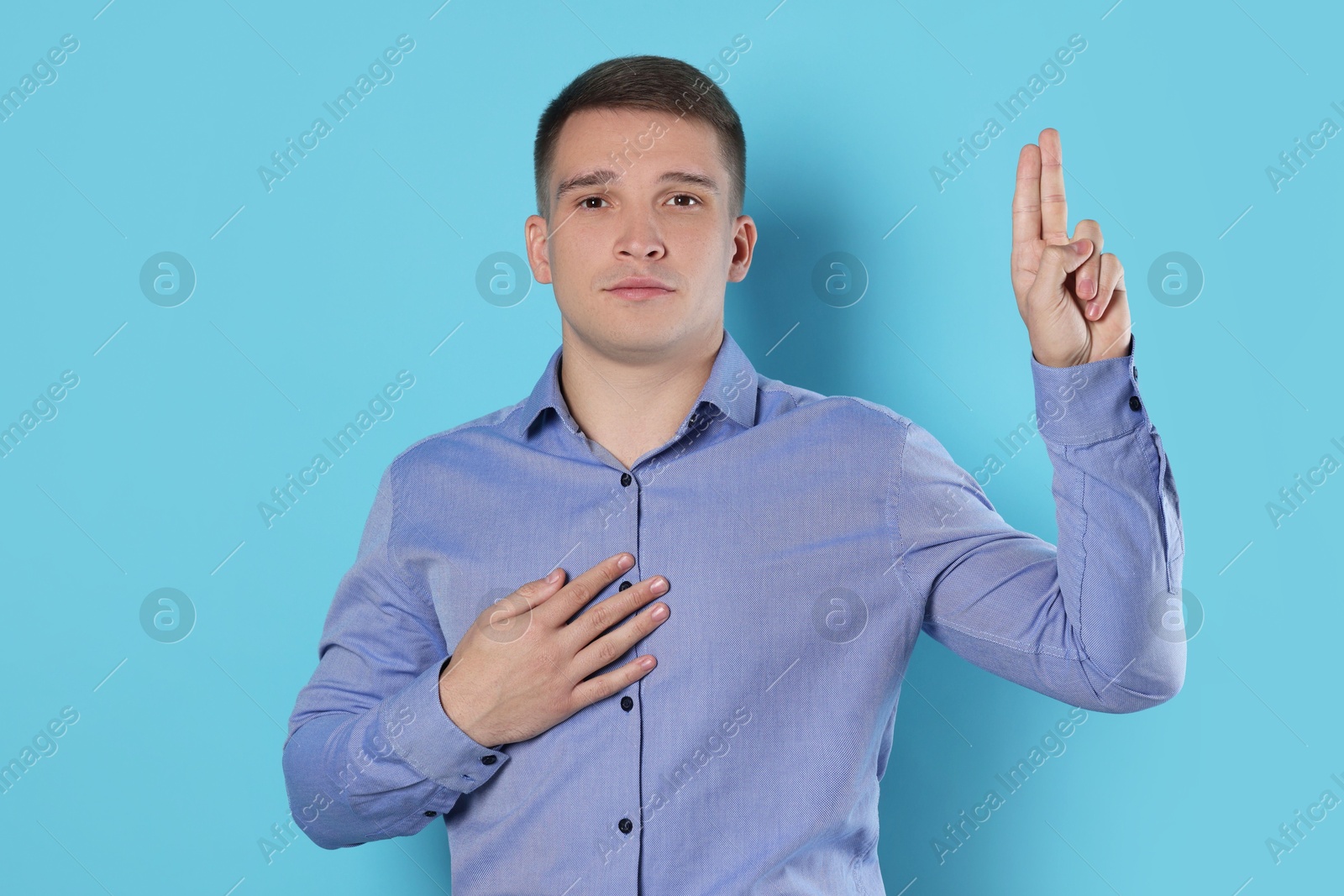 Photo of Man showing oath gesture on light blue background. Making promise