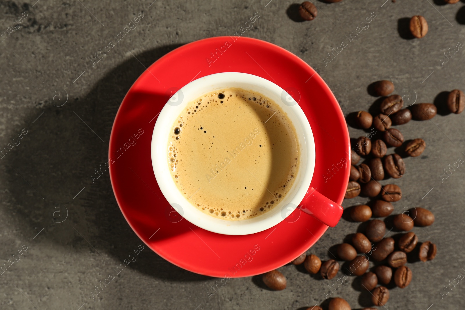 Photo of Red cup of aromatic coffee, saucer and beans on dark textured table, flat lay