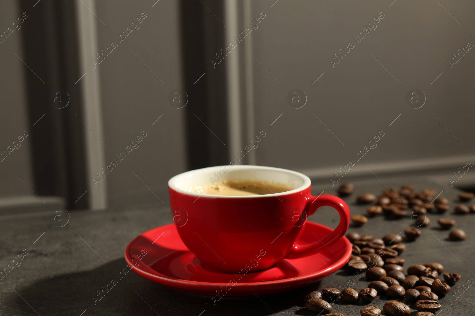 Photo of Red cup of aromatic coffee, saucer and beans on dark textured table, closeup