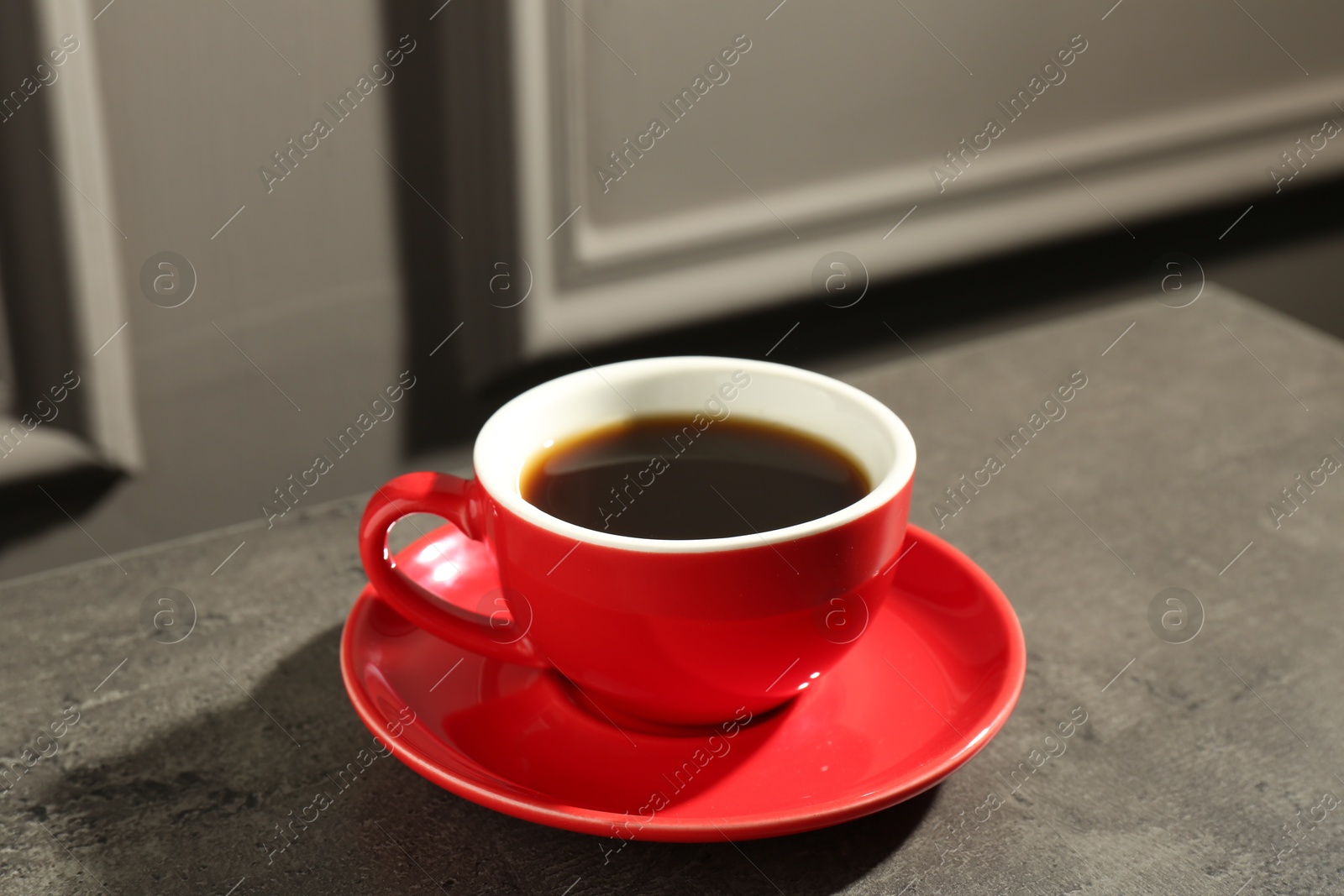 Photo of Red cup of aromatic coffee and saucer on dark textured table, closeup