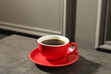 Photo of Red cup of aromatic coffee and saucer on dark textured table