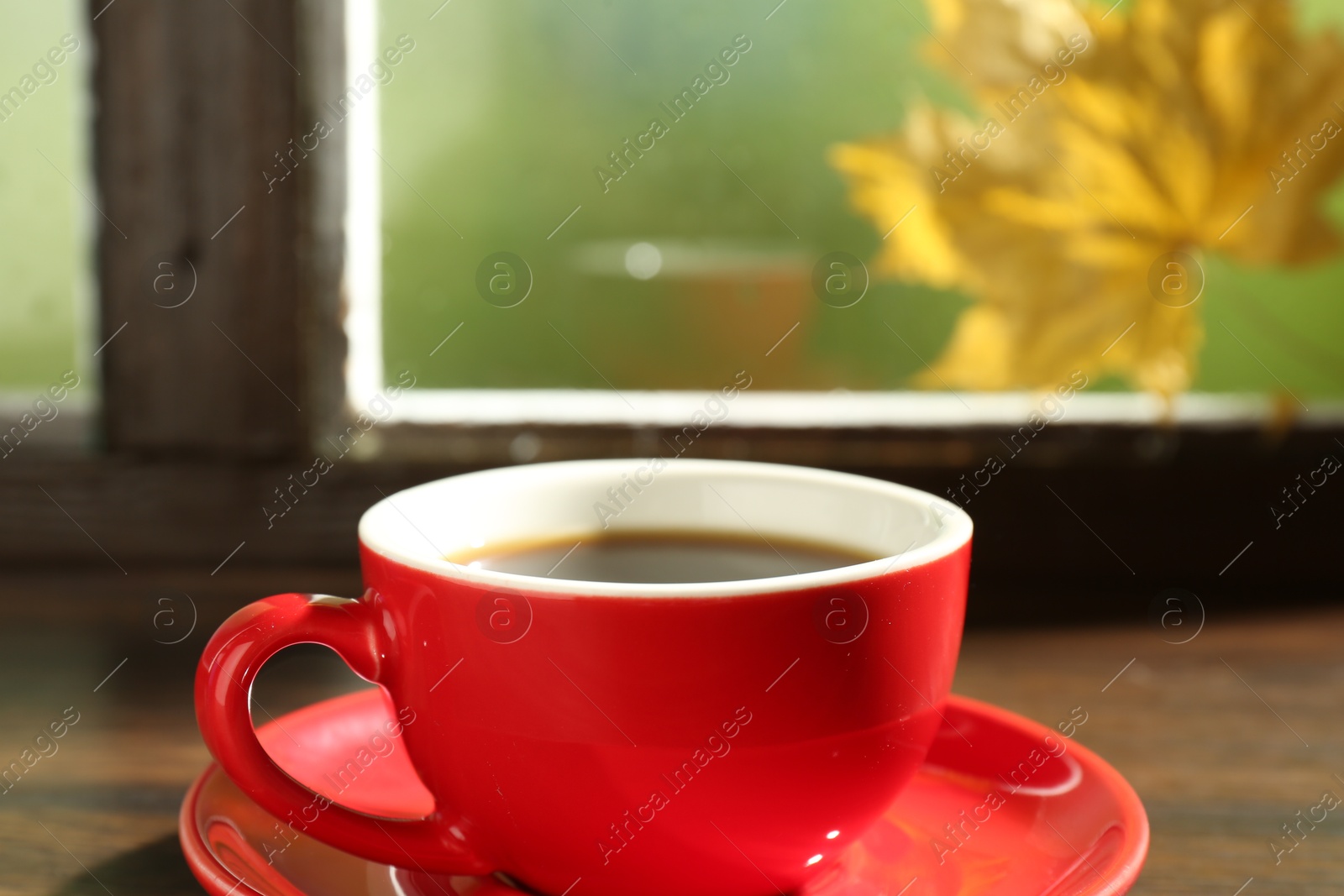 Photo of Red cup of aromatic coffee and saucer on wooden sill near window, closeup