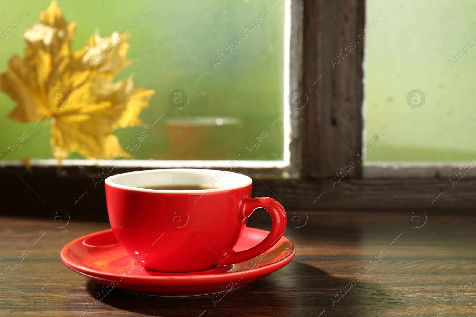 Photo of Red cup of aromatic coffee and saucer on wooden sill near window, closeup. Space for text