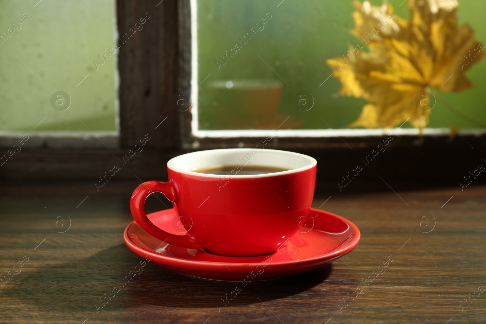 Photo of Red cup of aromatic coffee and saucer on wooden sill near window, closeup