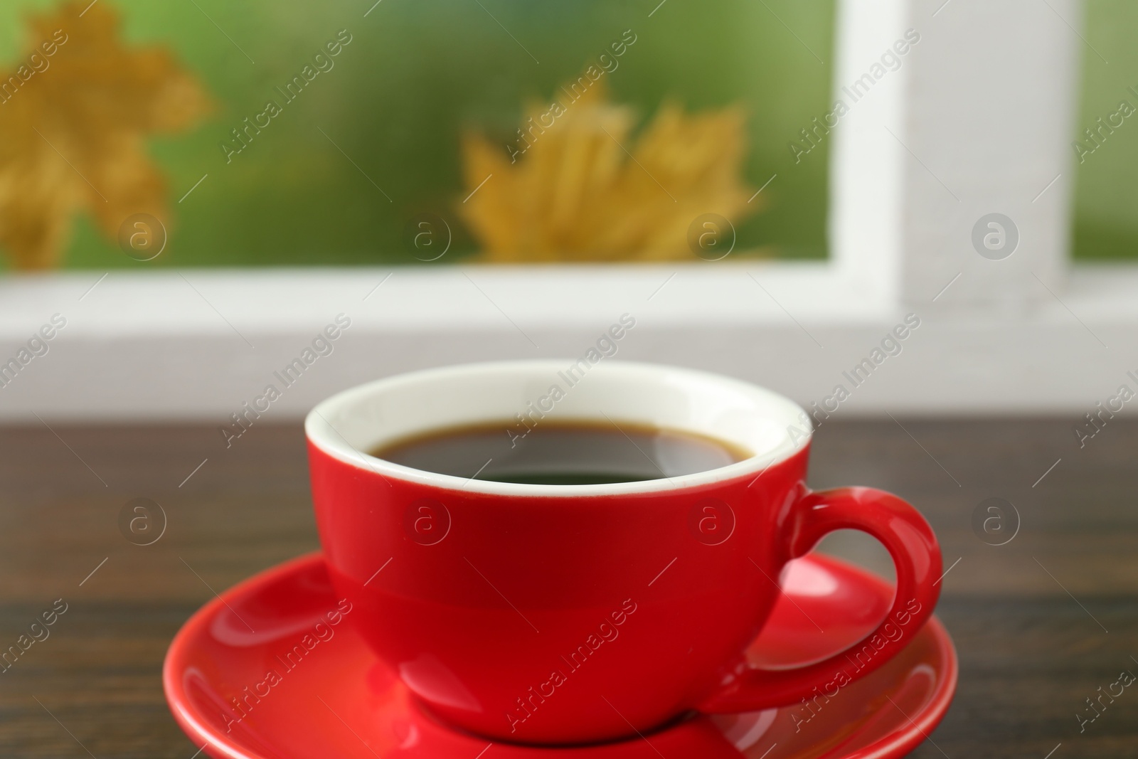 Photo of Red cup of aromatic coffee and saucer on wooden sill near window, closeup