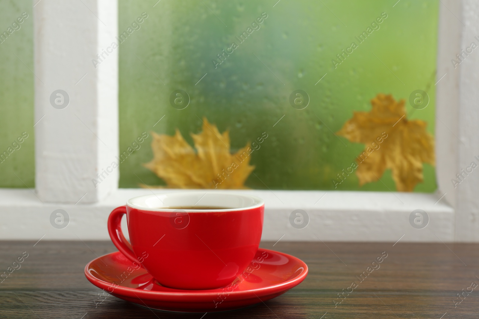 Photo of Red cup of aromatic coffee and saucer on wooden sill near window, closeup. Space for text