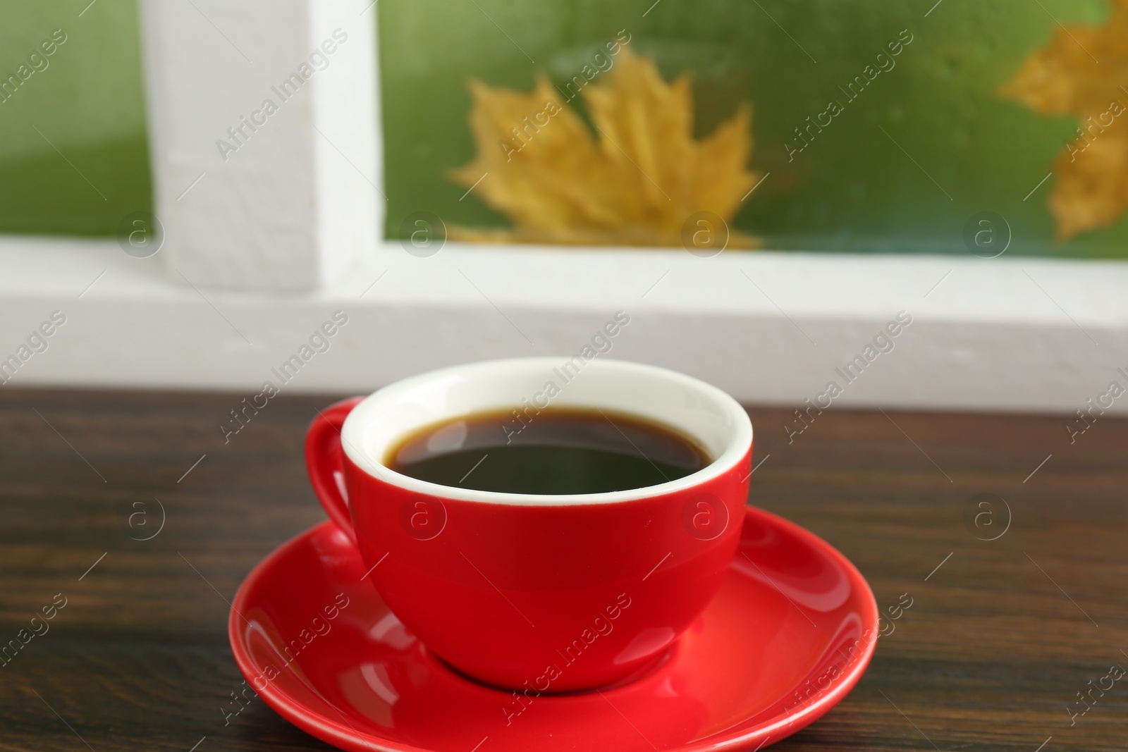 Photo of Red cup of aromatic coffee and saucer on wooden sill near window, closeup