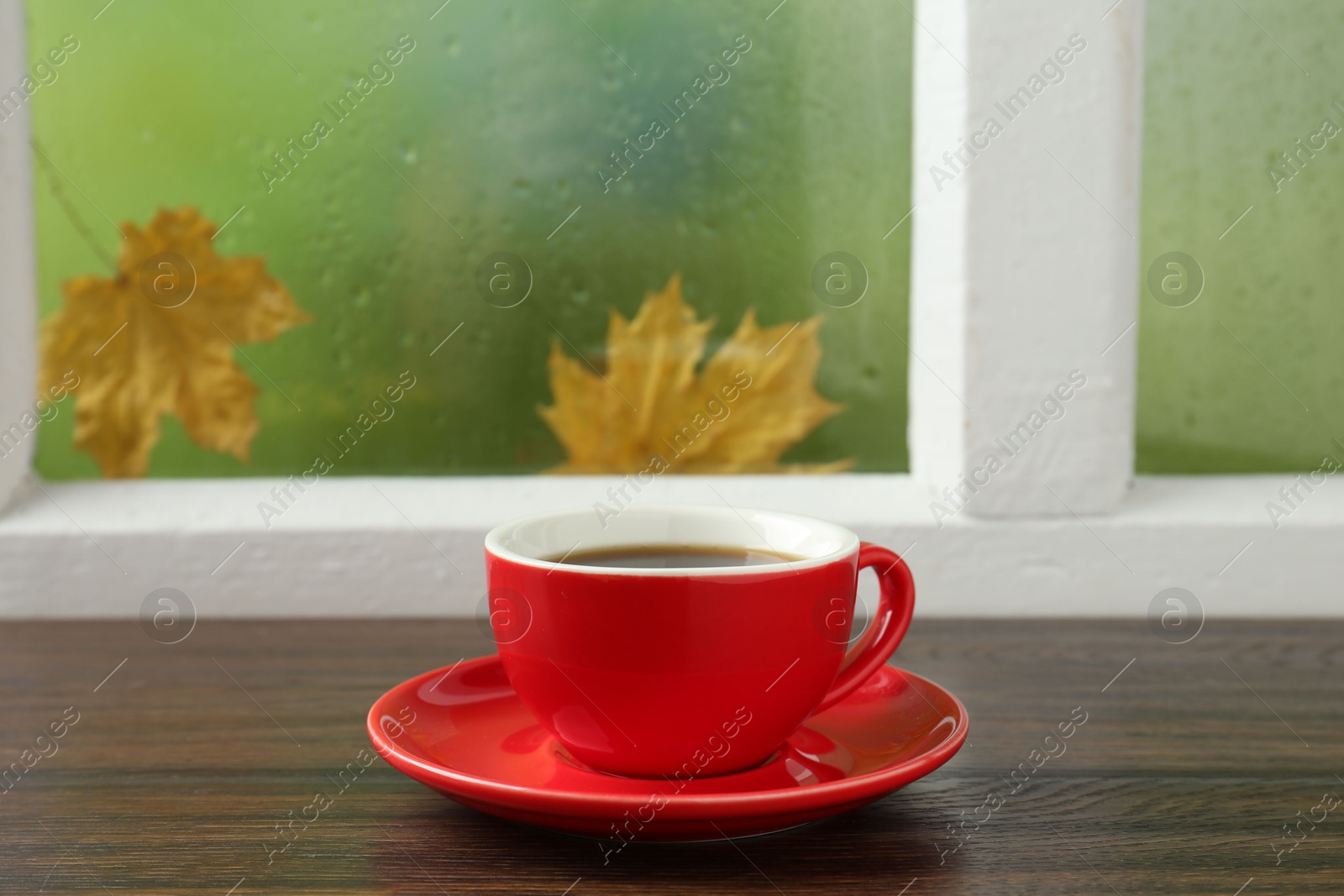 Photo of Red cup of aromatic coffee and saucer on wooden sill near window, closeup