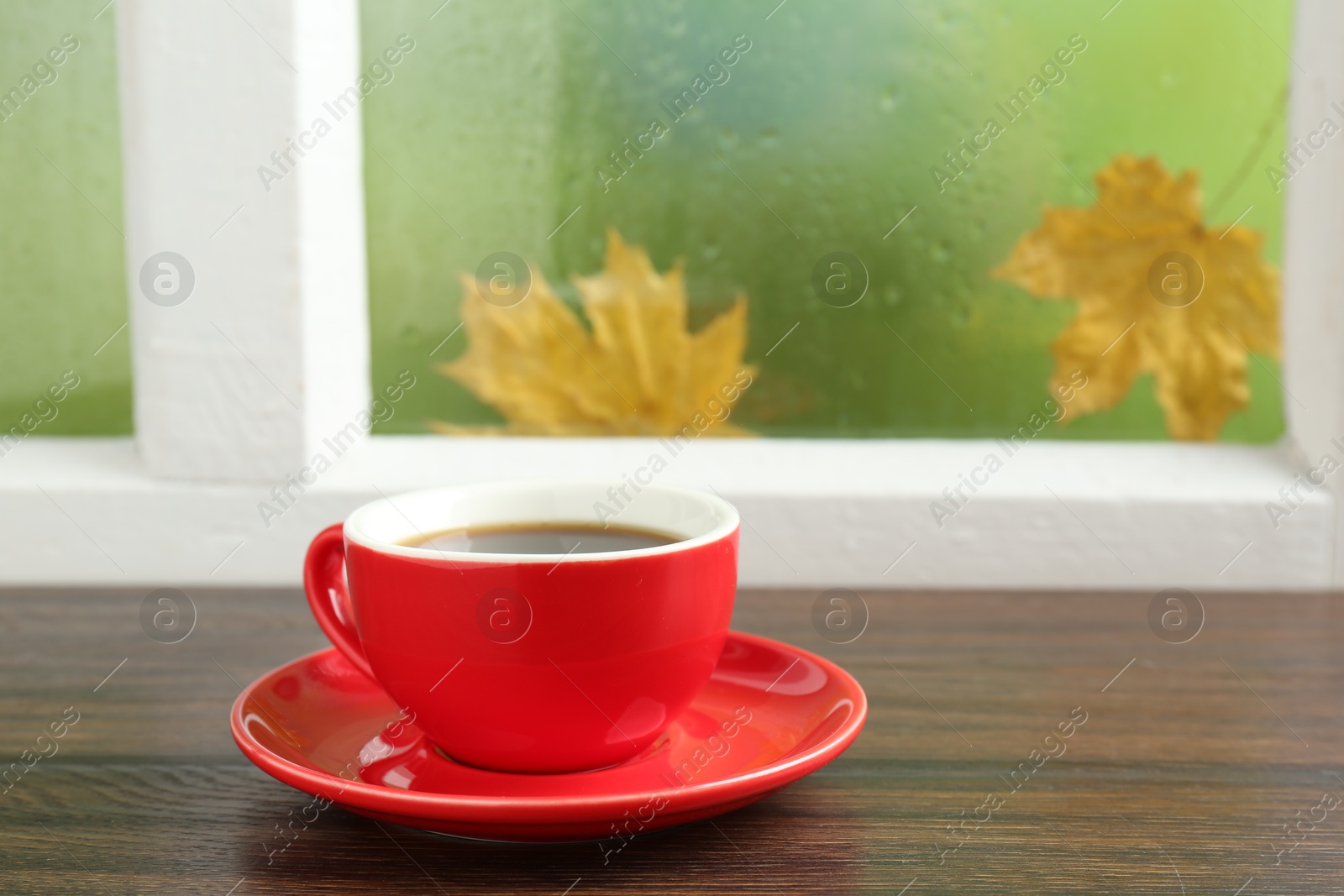 Photo of Red cup of aromatic coffee and saucer on wooden sill near window, closeup