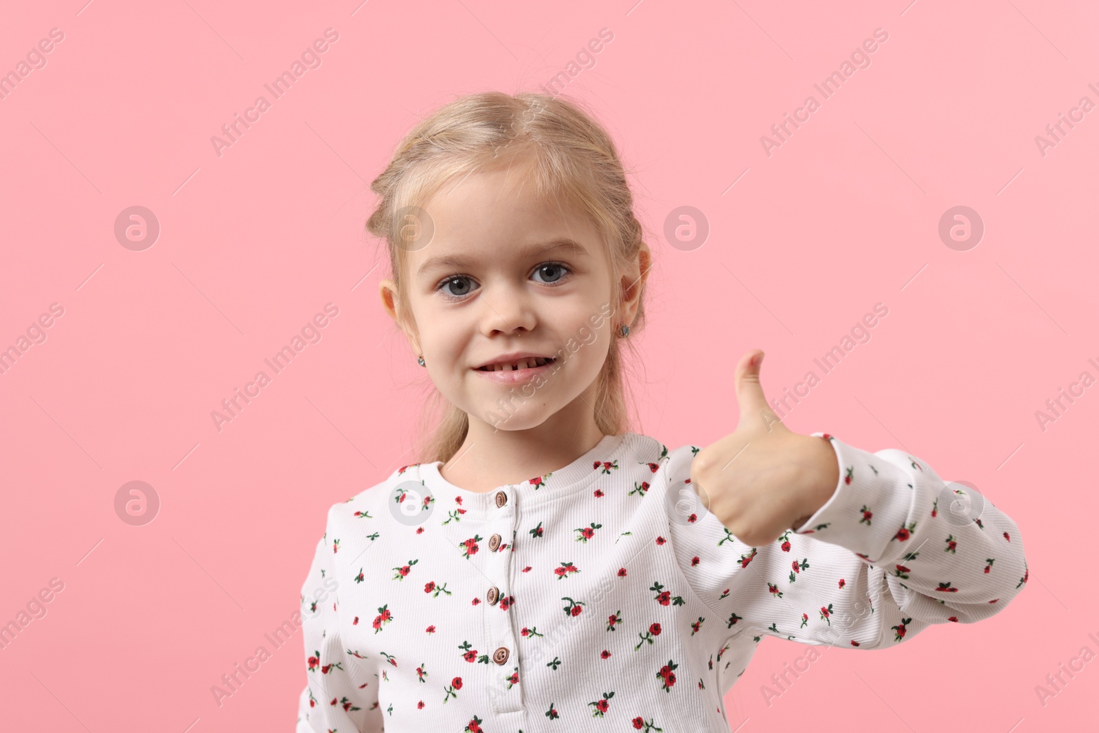 Photo of Cute little girl showing thumbs up on pink background