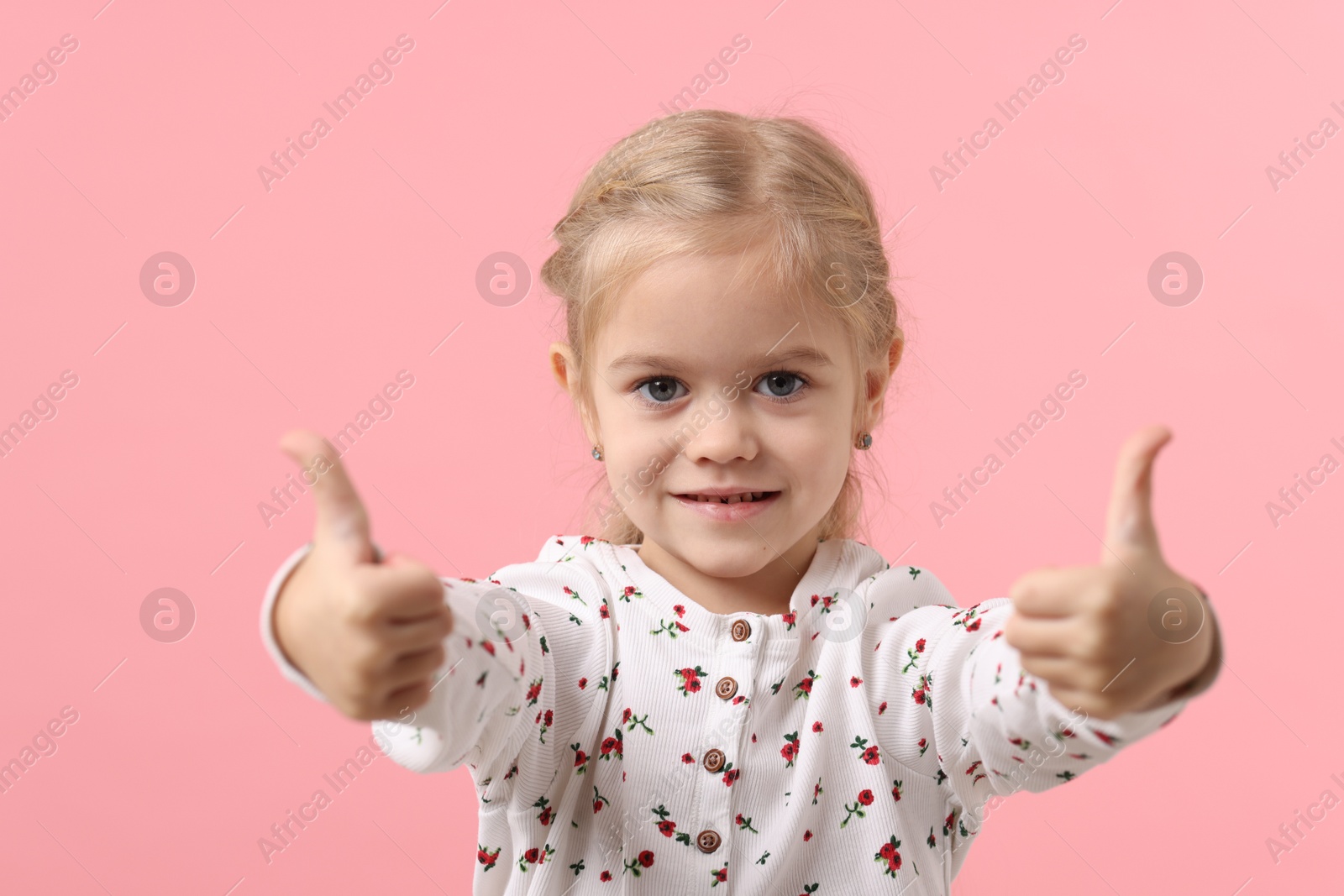 Photo of Cute little girl showing thumbs up on pink background