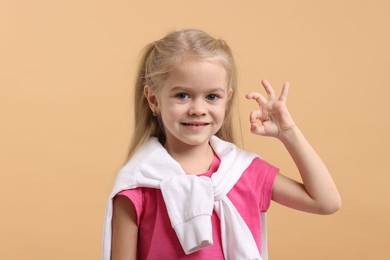 Photo of Cute little girl showing OK gesture on beige background