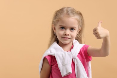 Photo of Cute little girl showing thumbs up on beige background, space for text