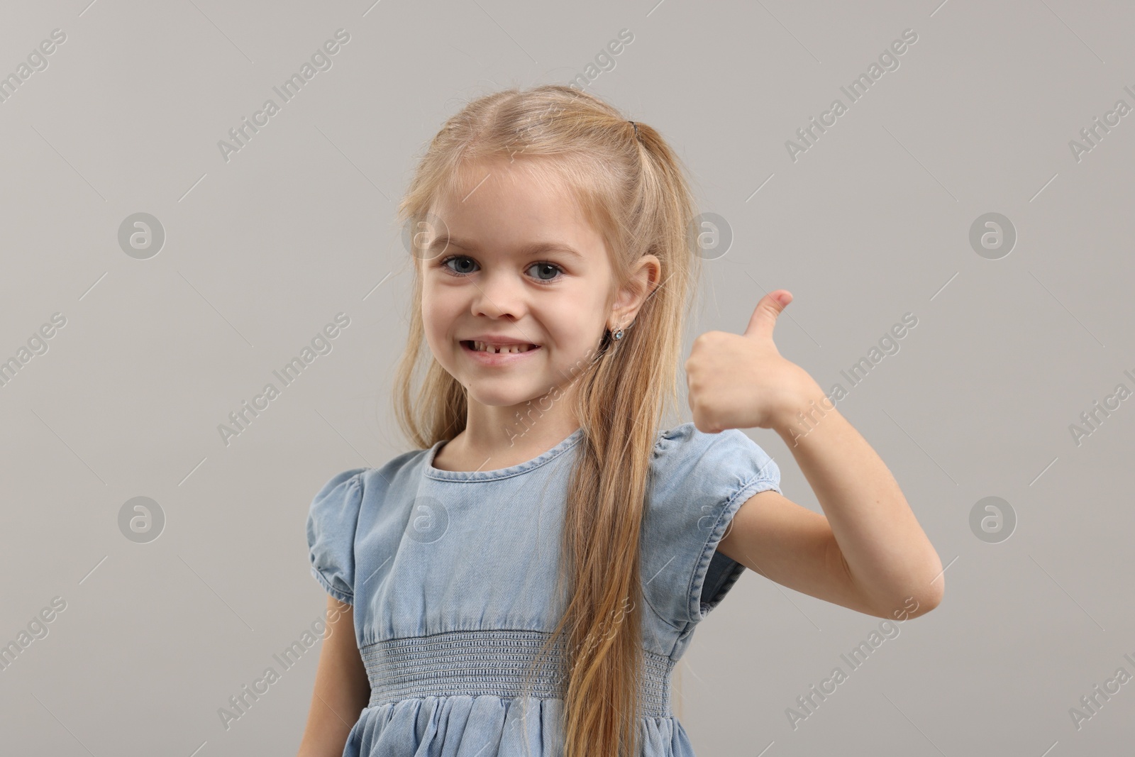 Photo of Cute little girl showing thumbs up on gray background