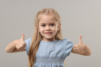 Photo of Cute little girl showing thumbs up on gray background