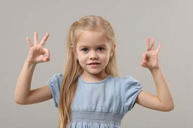 Photo of Cute little girl showing OK gesture on gray background