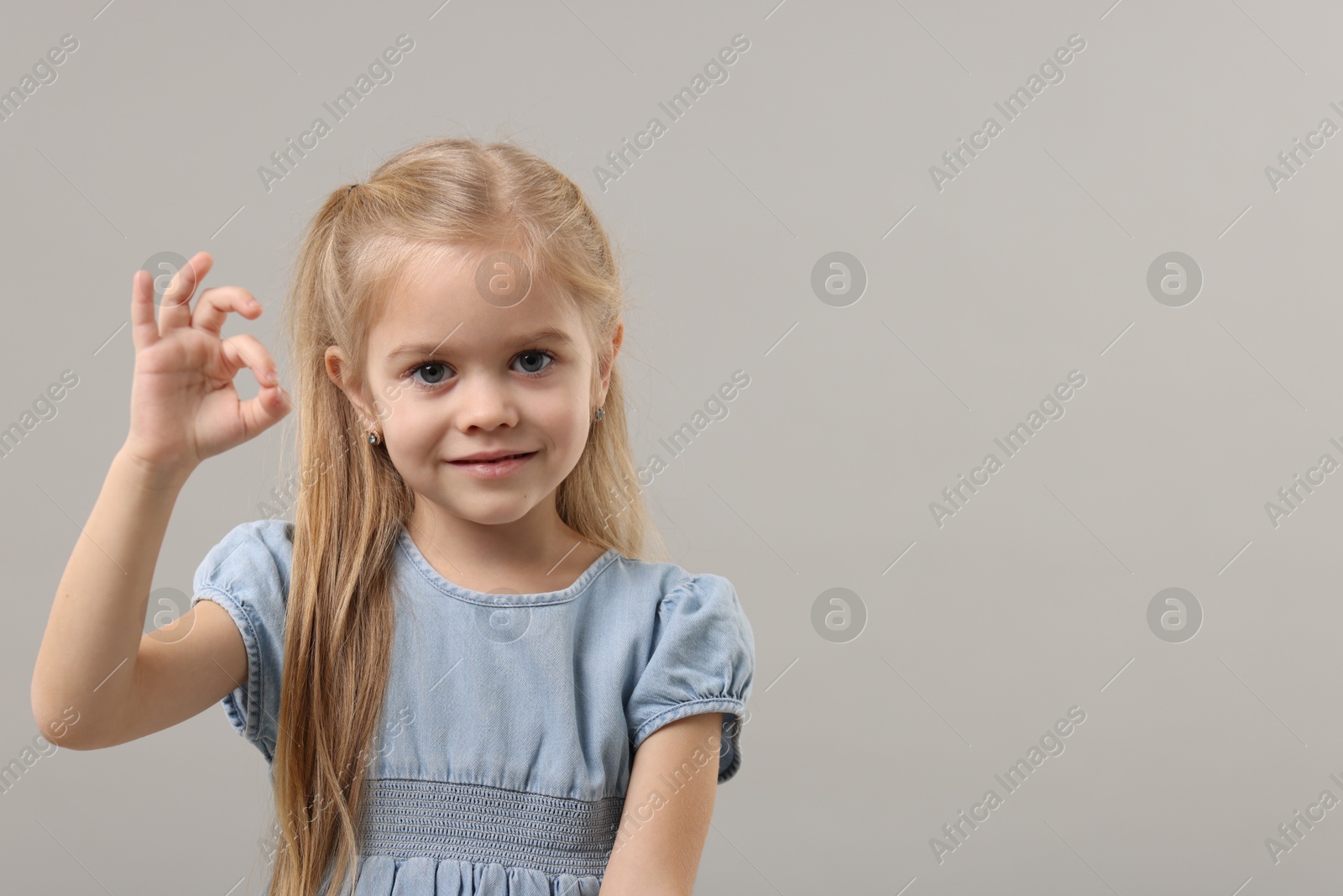 Photo of Cute little girl showing OK gesture on gray background. Space for text