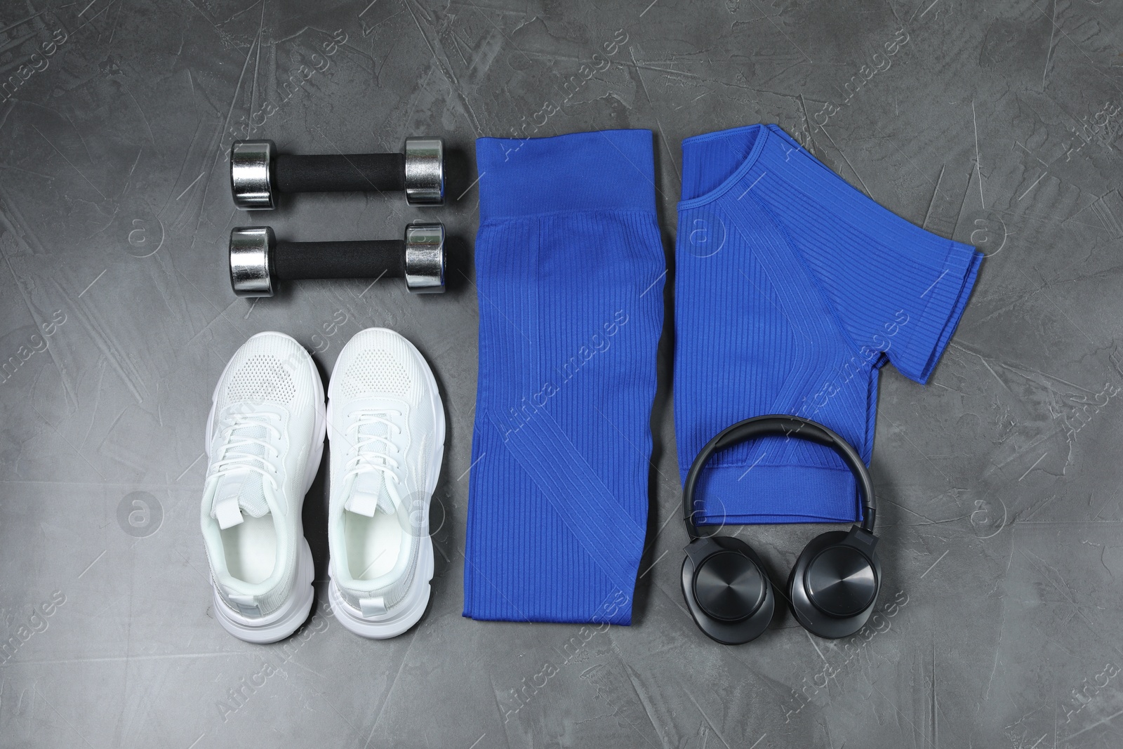 Photo of Stylish sportswear, white sneakers, dumbbells and headphones on grey background, flat lay