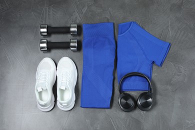 Photo of Stylish sportswear, white sneakers, dumbbells and headphones on grey background, flat lay