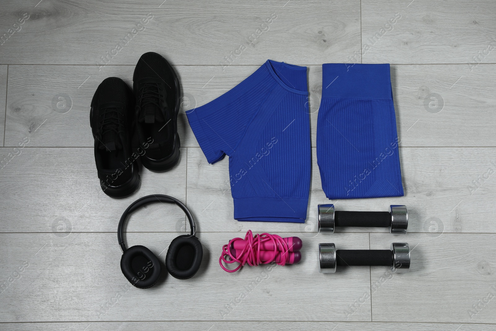 Photo of Stylish sportswear, black sneakers, dumbbells, skipping rope and headphones on wooden background, flat lay