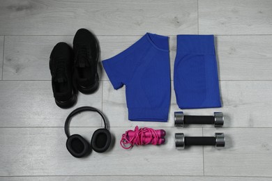 Photo of Stylish sportswear, black sneakers, dumbbells, skipping rope and headphones on wooden background, flat lay