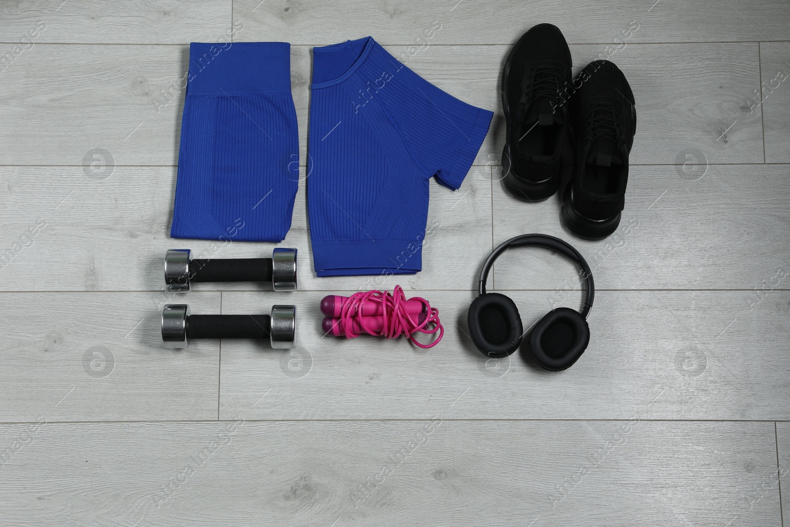 Photo of Stylish sportswear, black sneakers, dumbbells, skipping rope and headphones on wooden background, flat lay