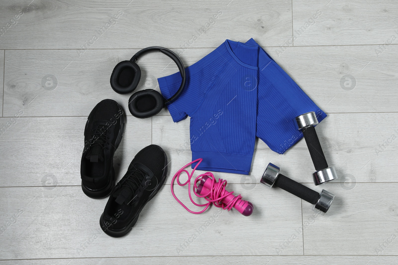 Photo of Stylish sportswear, black sneakers, dumbbells, skipping rope and headphones on wooden background, flat lay