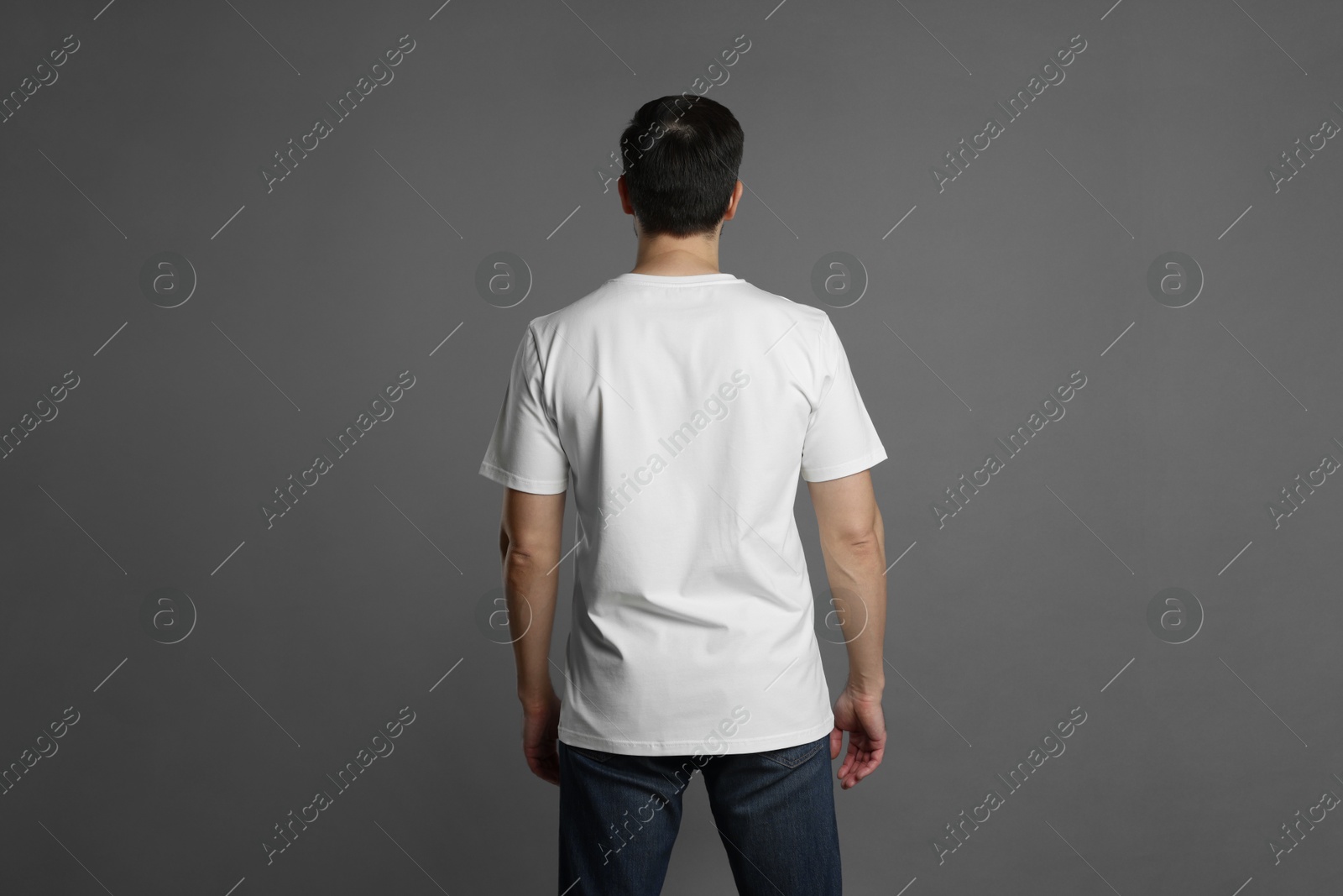 Photo of Man in blank white t-shirt on grey background, back view. Mockup for design