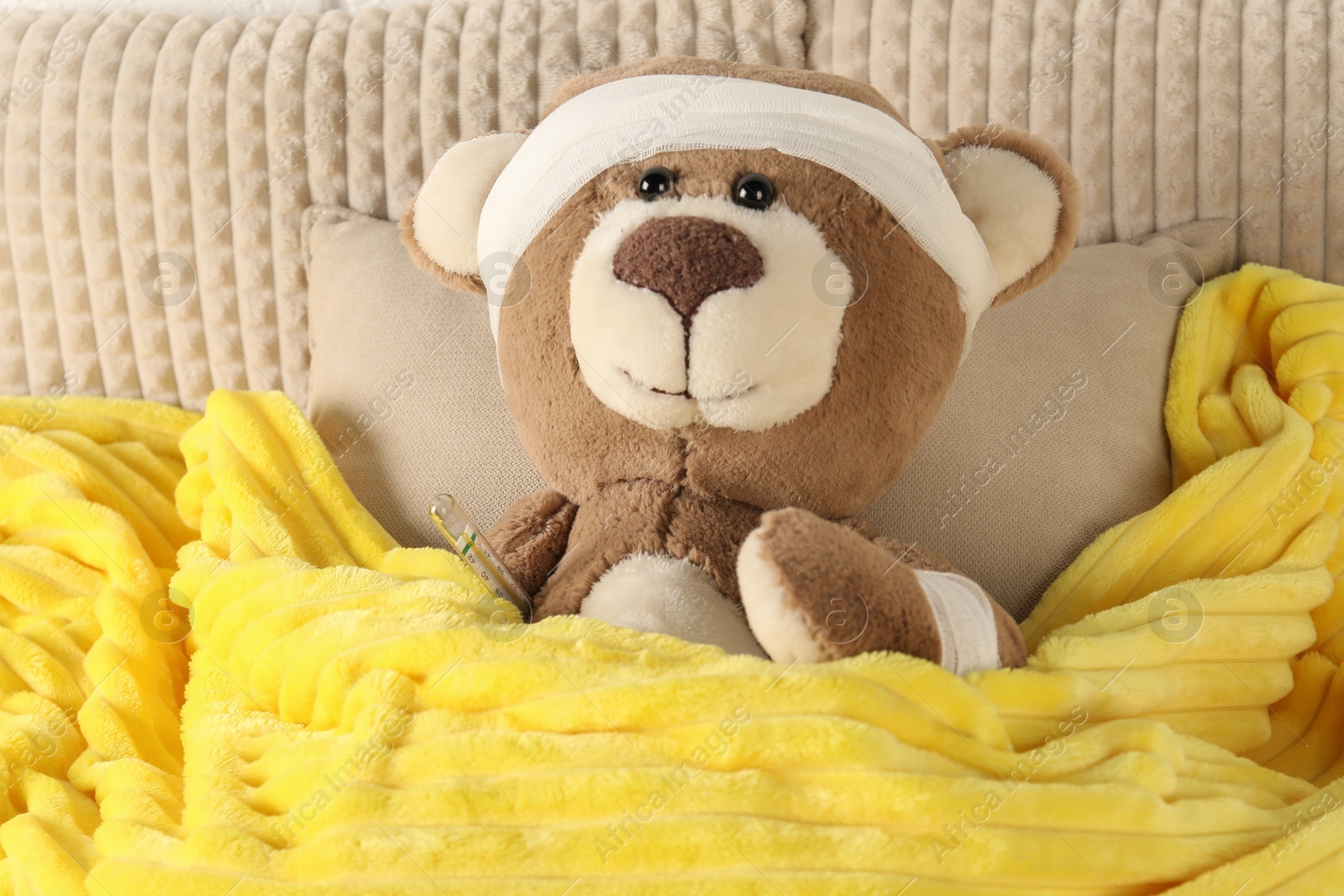 Photo of Cute teddy bear with bandages and thermometer on bed