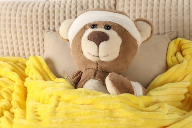 Photo of Cute teddy bear with bandages and thermometer on bed