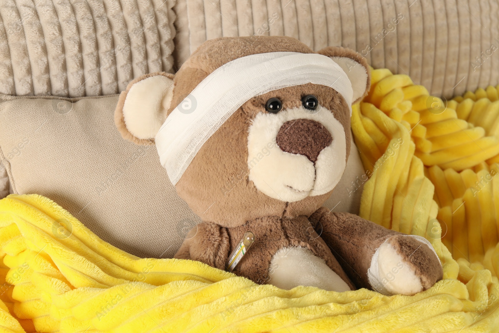 Photo of Cute teddy bear with bandage and thermometer on bed