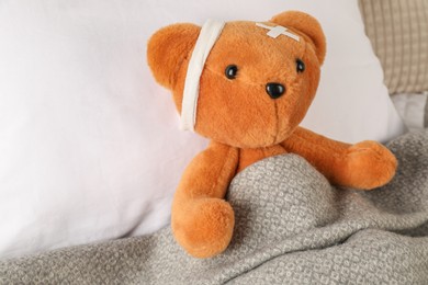 Photo of Cute teddy bear with bandage on bed