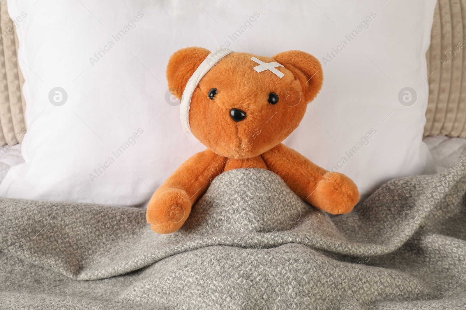 Photo of Cute teddy bear with bandage and adhesive medical plasters on bed, top view