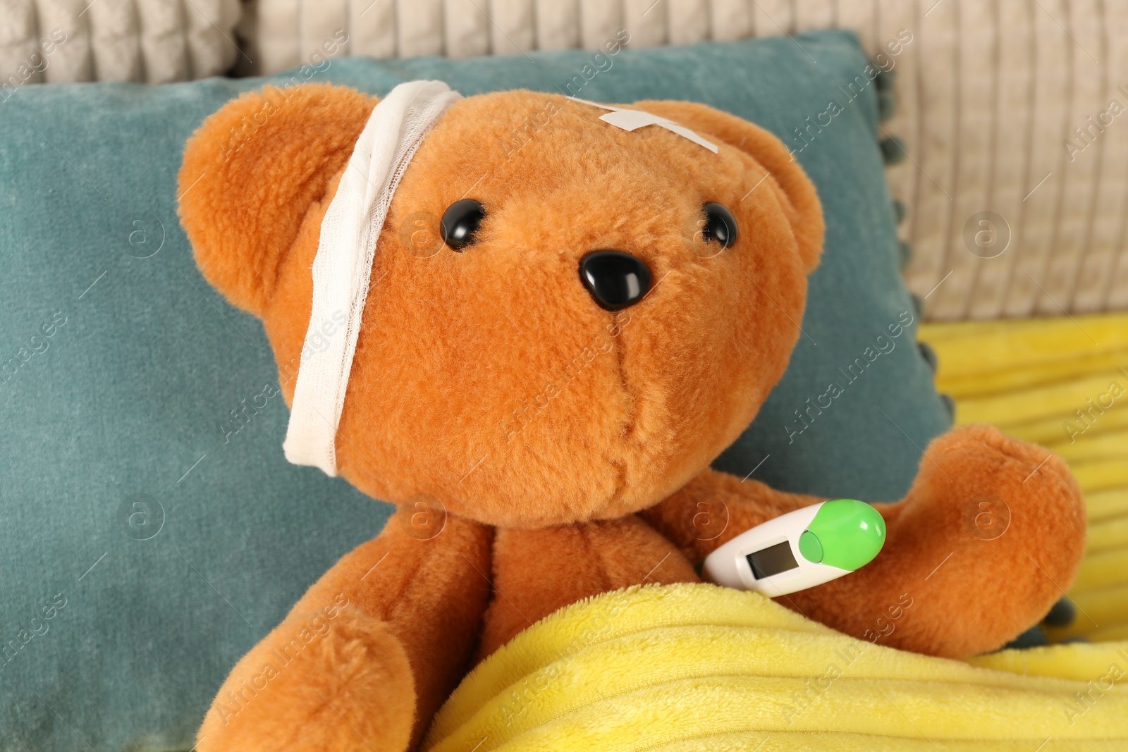 Photo of Cute teddy bear with bandage, adhesive medical plasters and thermometer on bed