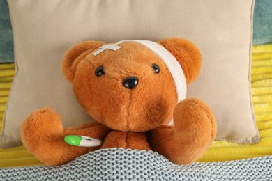 Photo of Cute teddy bear with bandage, adhesive medical plasters and thermometer on bed, top view