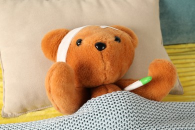 Photo of Cute teddy bear with bandage, adhesive medical plasters and thermometer on bed